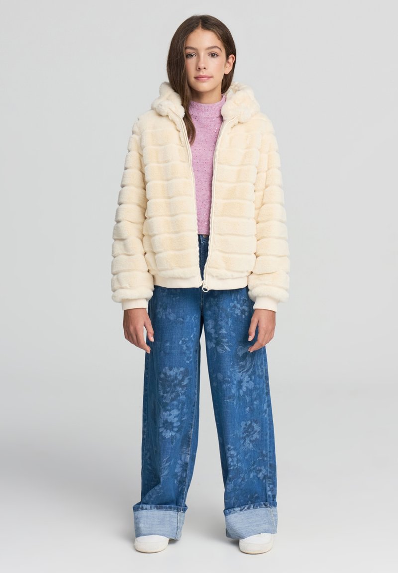Kremowa kurtka z futra sztucznego na zamek z kapturem, z pikowanym wzorem. W połączeniu z szerokimi niebieskimi dżinsami w kwiatowe wzory i podwiniętymi nogawkami.