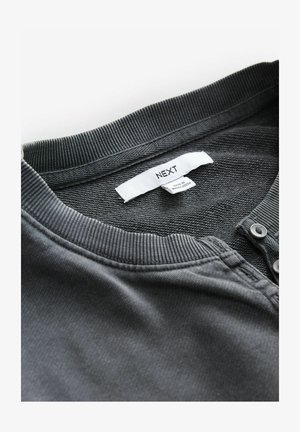 Ciemnoszara bawełniana koszula z prążkowanym kołnierzykiem, dwiema guzikami i subtelną teksturą. Metka z napisem "NEXT" zawiera informacje o pielęgnacji.