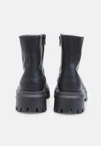 Crne kožne čizme do članaka s debelim, rebrastim đonom. Bočno zatvaranje na patentni zatvarač, glatka tekstura i minimalni detalji šivanja.