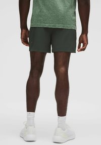 Herrars mörkgröna sportshorts, lättviktig tyg, längd till mitten av låret, i kombination med vita sneakers och strumpor, med en strukturerad grön tröja.