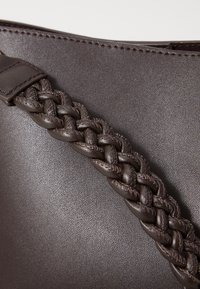 Sac à main en cuir marron avec une finition texturée. Équipé d'une sangle tressée fixée avec des accents en cuir plat et lisse.