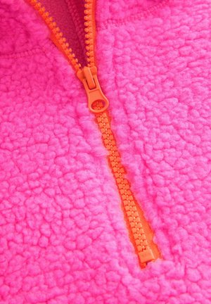 Fleece-pullover i stark rosa med en texturerad yta, med en orange dragkedja och sömdetaljer längs kanterna.