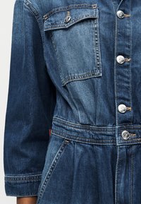 Τζιν μπουφάν με ασημένια κουμπιά, τσέπη με καπάκι στο στήθος, πλαϊνές τσέπες ραφής και σφηκοφωλιά στη μέση στα μακριά μανίκια.