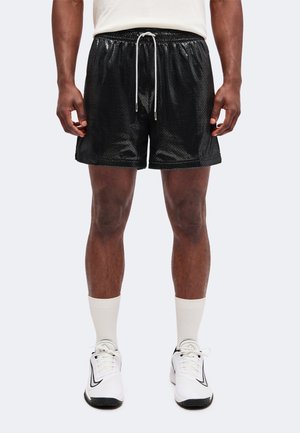 Homme portant un short en mesh noir avec un cordon blanc, des chaussettes blanches et des chaussures de sport blanches avec un logo swoosh noir.