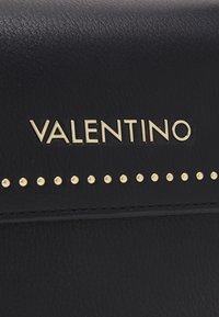Borsa a tracolla in pelle nera con logo dorato "VALENTINO" e una fila di borchie dorate lungo il bordo, con superficie texture e dettagli cuciti.