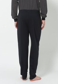 Schwarze, weiche Stoffhosen mit elastischem Bund, gerader Schnitt und lässiger Passform. Getragen mit einem gemusterten Langarmshirt.