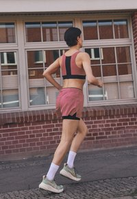 Athletic outfit featuring a pink and black sports bra and matching shorts with black trim. Wearing green running shoes and white socks.