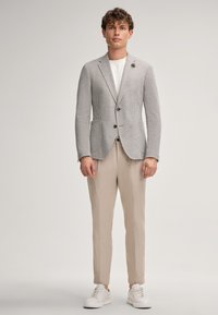 Heren lichtgrijs gestructureerd colbert met verticale strepen, twee knopen en twee voorknochelzakken, gecombineerd met beige tapered broek en witte sneakers.