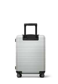 Silver hard-shell suitcase with horizontal ridges, black handle, and four wheels for mobility. Compact and sturdy design for travel.
