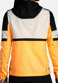 Colorful windbreaker with a black hood, vibrant orange body, and gray accents. Features reflective strips and a cropped design.