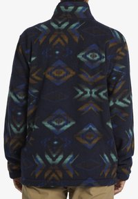 Fleece-Pullover mit marineblauem Hintergrund und mehrfarbigem geometrischem Muster, das Farbtöne von Blau, Grün, Braun und einen verstellbaren Kragen aufweist.