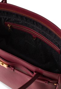 Burgundy leather handbag interior with a textured black lining. Features a zip pocket and gold hardware accents.
