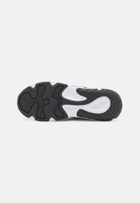 Semelle d'une chaussure de sport blanche et noire avec des rainures texturées et des motifs courbés pour l'adhérence et le soutien.