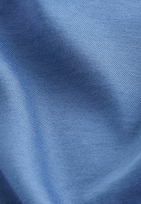 Modrá bavlněná látka s hladkým povrchem, s jemným žebrovaným vzorem. Materiál je lehký a flexibilní, měkce se splétá.