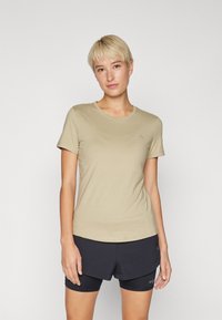 T-shirt beige clair à manches courtes avec un col rond. Tissu doux, design ajusté, avec un logo discret sur la poitrine gauche.