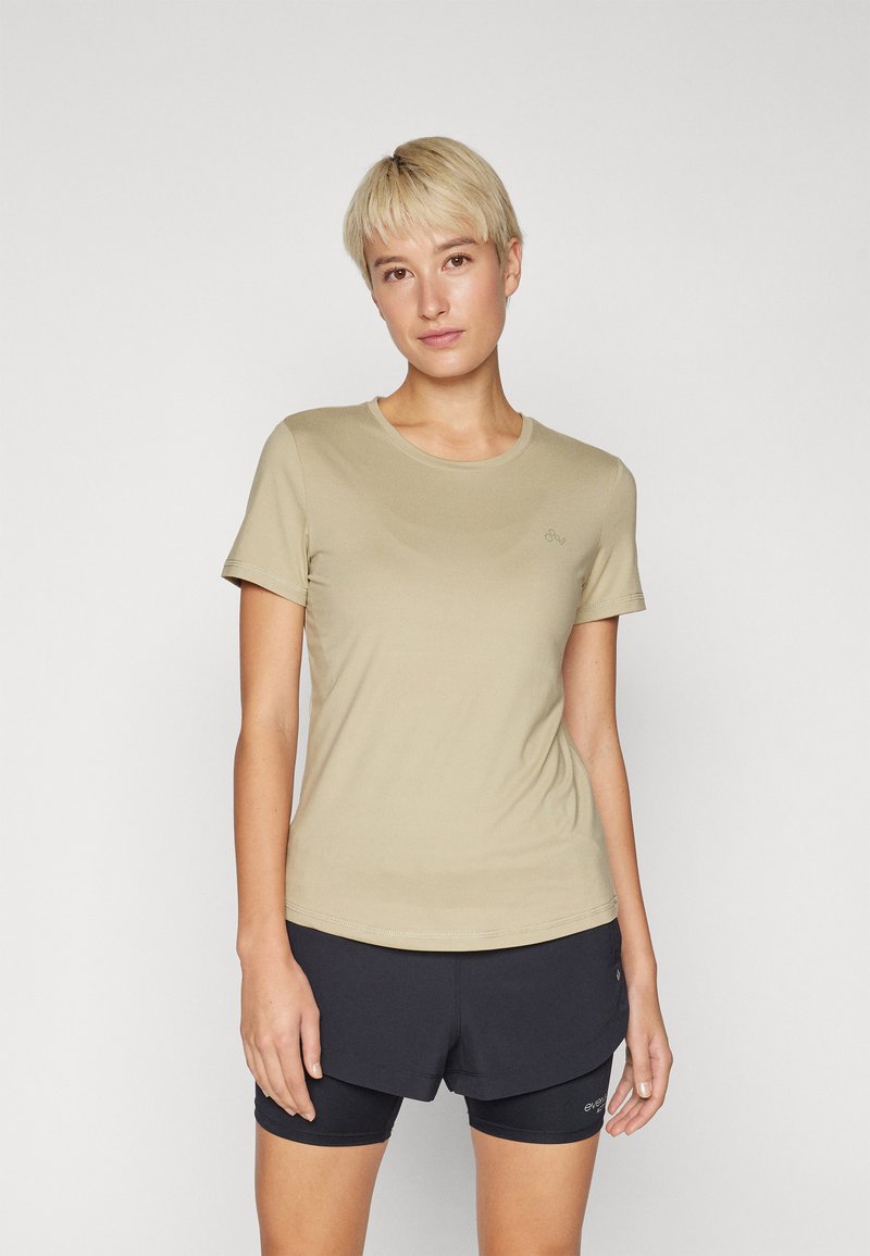 T-shirt beige clair à manches courtes avec un col rond. Tissu doux, design ajusté, avec un logo discret sur la poitrine gauche.