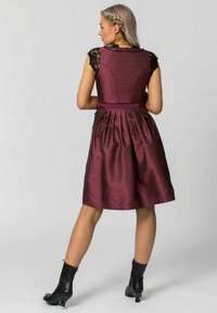 Burgunderfarbenes Kleid mit strukturierter Corsage, kurzen Spitzenärmeln und plissiertem Rock. Abgerundet mit einem passenden Taillengürtel und getragen mit schwarzen Knöchelstiefeln.
