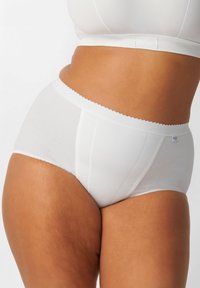 Persona curvy che indossa biancheria intima bianca in cotone a vita alta e un reggiseno bianco abbinato, su uno sfondo bianco uniforme.