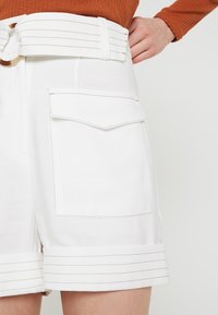 Vita shorts med en bred, bälteskant, som har sidofickor och upprullad nederkant med subtila sömdekor.