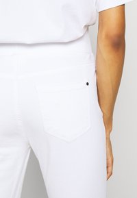 Pantalones vaqueros de mezclilla blanca con un diseño clásico de bolsillo trasero con un pequeño remache negro, tejido texturizado y una silueta ajustada.