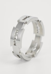 Inel argintiu cu un design segmentat, având decupaje geometrice, suprafață netedă și lustruită, și detalii texturate pe banda interioară.