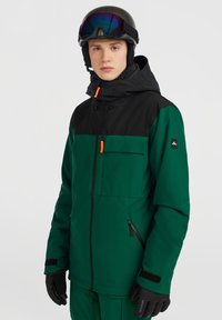 Grøn og sort skijakke med hætte, frontlomme og orange lynlåsdetalje. Glat tekstur, forstærkede sømme, designet til brug ved vintersport.