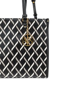 Borsa a tote nera con un motivo geometrico bianco. Presenta un charm con logo dorato e manici neri lisci. Tessuto texture e dettagli dorati.