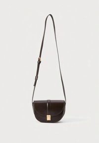 Brūna ādas plecu soma ar apaļu aizdares vāciņu, zelta krāsas aizslēgu un regulējamu siksnu. Raksturīga kontrastējoša šuvuma un gluda tekstūra.