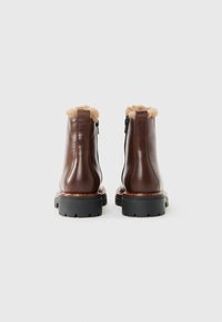 Une paire de bottes en cuir marron montantes avec des semelles épaisses noires et une doublure en fourrure beige visible en haut, vue de l'arrière.