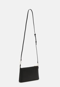 Borsa a tracolla nera in pelle con tracolla sottile regolabile e hardware in tono argento, mostrata appesa su uno sfondo bianco semplice.