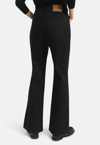 Jean noir évasé en denim avec deux poches arrière et une patch en cuir marron à la taille. Fini mat avec un ourlet droit.