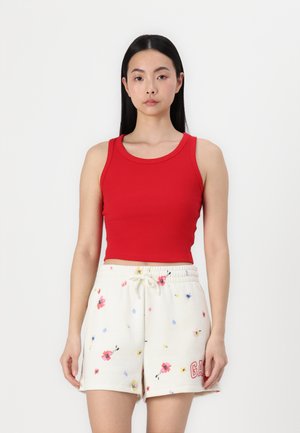 Rode geribbelde crop tanktop gecombineerd met crèmekleurige shorts met een bloemenpatroon en een trekkoord. De shorts hebben een rood logo aan de zijkant.