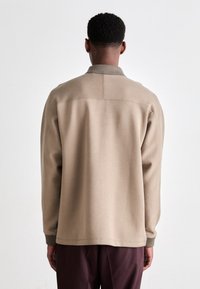 Beige sweatshirt with a collar, ribbed cuffs, and hem. Features a smooth texture, relaxed fit, with minimal stitching details at the back.