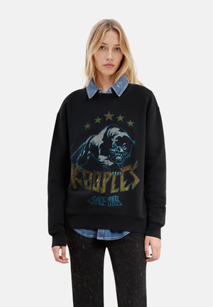 Felpa nera con un design grafico di un pantera e scritta dorata "KOOPLES." Presenta un collo a costine e una camicia di denim a strati sotto.