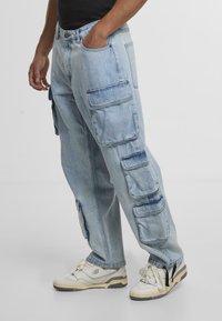 Lyseblå denim cargo-bukser med flere sidelommer, afslappet pasform og opsmøgede ben, parret med hvide sneakers.