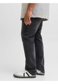 Vaqueros de mezclilla negros con corte recto, combinados con zapatillas blancas y grises que tienen rayas negras. La tela parece tener textura.