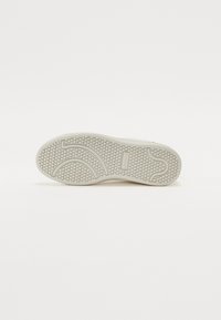 Sål av sko med en teksturert gummioverflate, med et heksagonalt mønster og buede linjer. Fargen er for det meste lys beige med subtile detaljer.