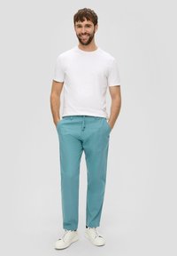 Lichtblauwe broeken met een relaxte pasvorm, gemaakt van zachte stof, met een elastische tailleband en een drawstring. Gecombineerd met een wit t-shirt en witte sneakers.