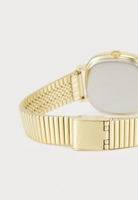 Montre Casio dorée avec un boîtier rectangulaire, un bracelet en métal texturé au design en maille et un fermoir portant le nom de la marque gravé.