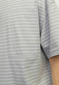 Hallitusgray lühikeste varrukatega särk, millel on valged horisontaalsed triibud, vasakul rinna peal tasku ja pehme, kergesti liikuv kangas.
