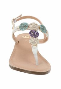 Tongs blanches avec une bride transparente, ornées de quatre accents en pierres précieuses turquoise, violet, transparent et argenté. Semelle lisse beige.