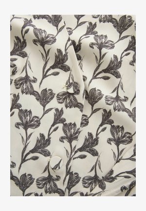 Kremveida audums ar melnu ziedu rakstu, kurā ir auduma pogas un redzamās šuves salocītajā daļā.