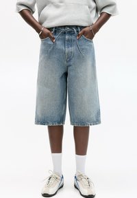 Shorts Bermuda en denim bleu clair avec une coupe relaxée, dotés d'une taille à cordon, de poches latérales et d'un ourlet brut.
