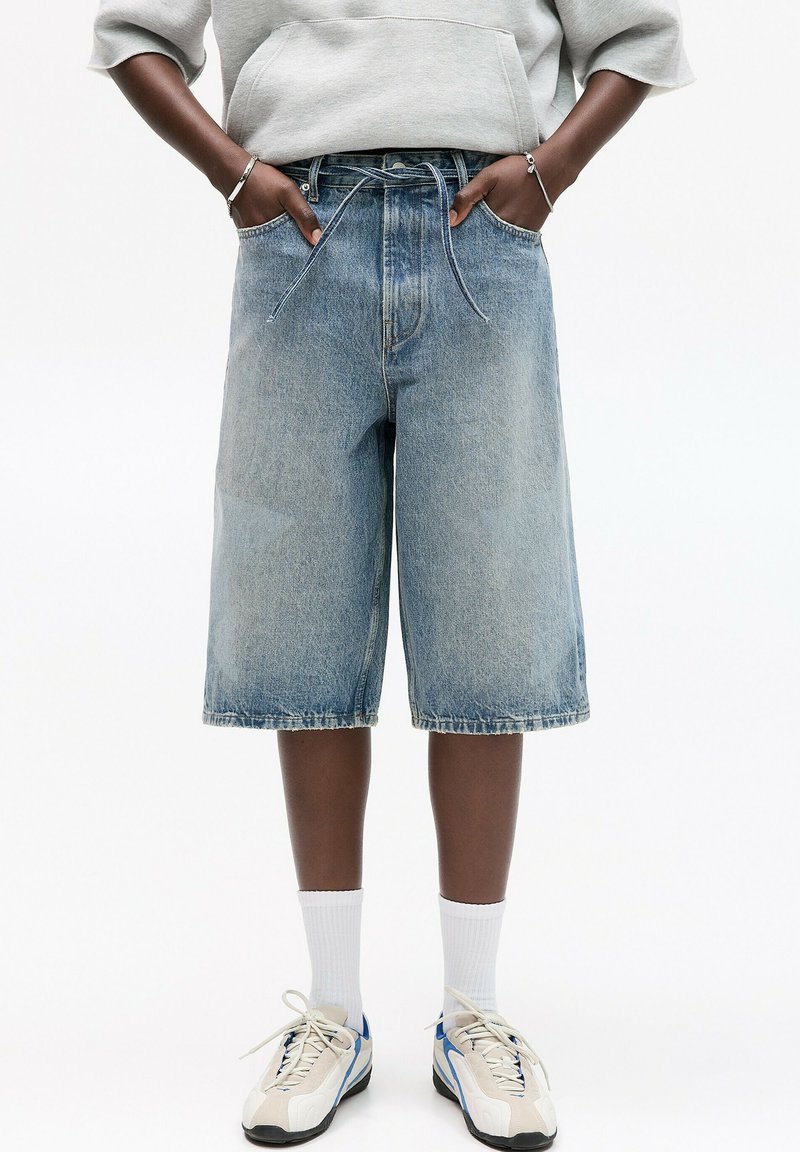 Shorts Bermuda en denim bleu clair avec une coupe relaxée, dotés d'une taille à cordon, de poches latérales et d'un ourlet brut.