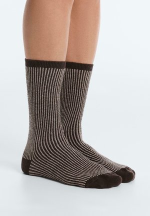 Noge u srednjoj dužini čarapa rebrastog uzorka s tamnosmeđim prstima, petama i rubovima, s izmjeničnim tamnim i svijetlim okomitim prugama.