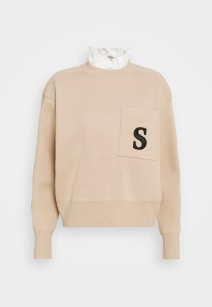 Pull beige à manches longues avec poignets côtelés, une poche poitrine ornée d'un "S" noir, et un détail de col blanc à volants.