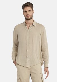 Camicia a maniche lunghe in lino beige con chiusura a bottoni, vestibilità rilassata e colletto appuntito. Leggera texture con dettagli sottili.