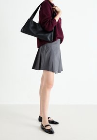 Sac à bandoulière en cuir noir, pull en maille bordeaux, jupe plissée grise et ballerines en cuir verni noir avec un d étail de boucle.