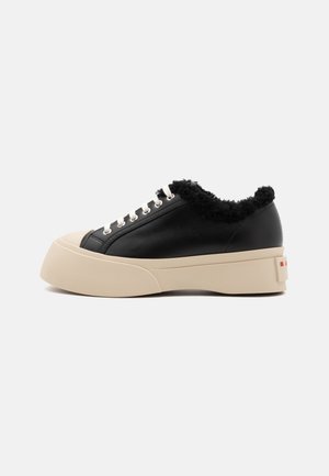 Baskets en cuir noir avec une épaisse semelle plateforme beige, dotées d'un col noir en fourrure et de lacets blancs, avec un accent de marque sur le talon.