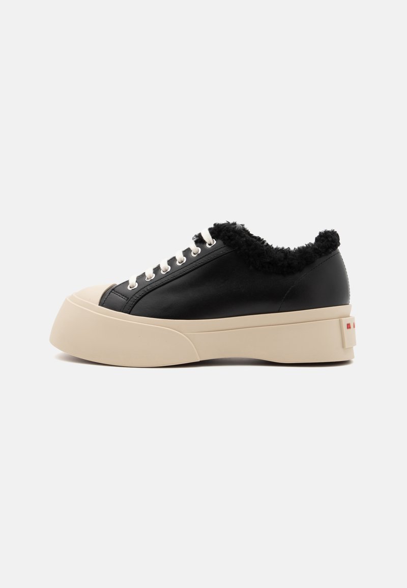 Black leather sneaker with a thick beige platform sole, featuring a fuzzy black collar and white laces, with a branded accent on the heel.